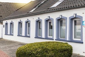 A building with a row of arched windows and a small hedge in front. - 50111 Fisherman's Loft (Carolinensiel)