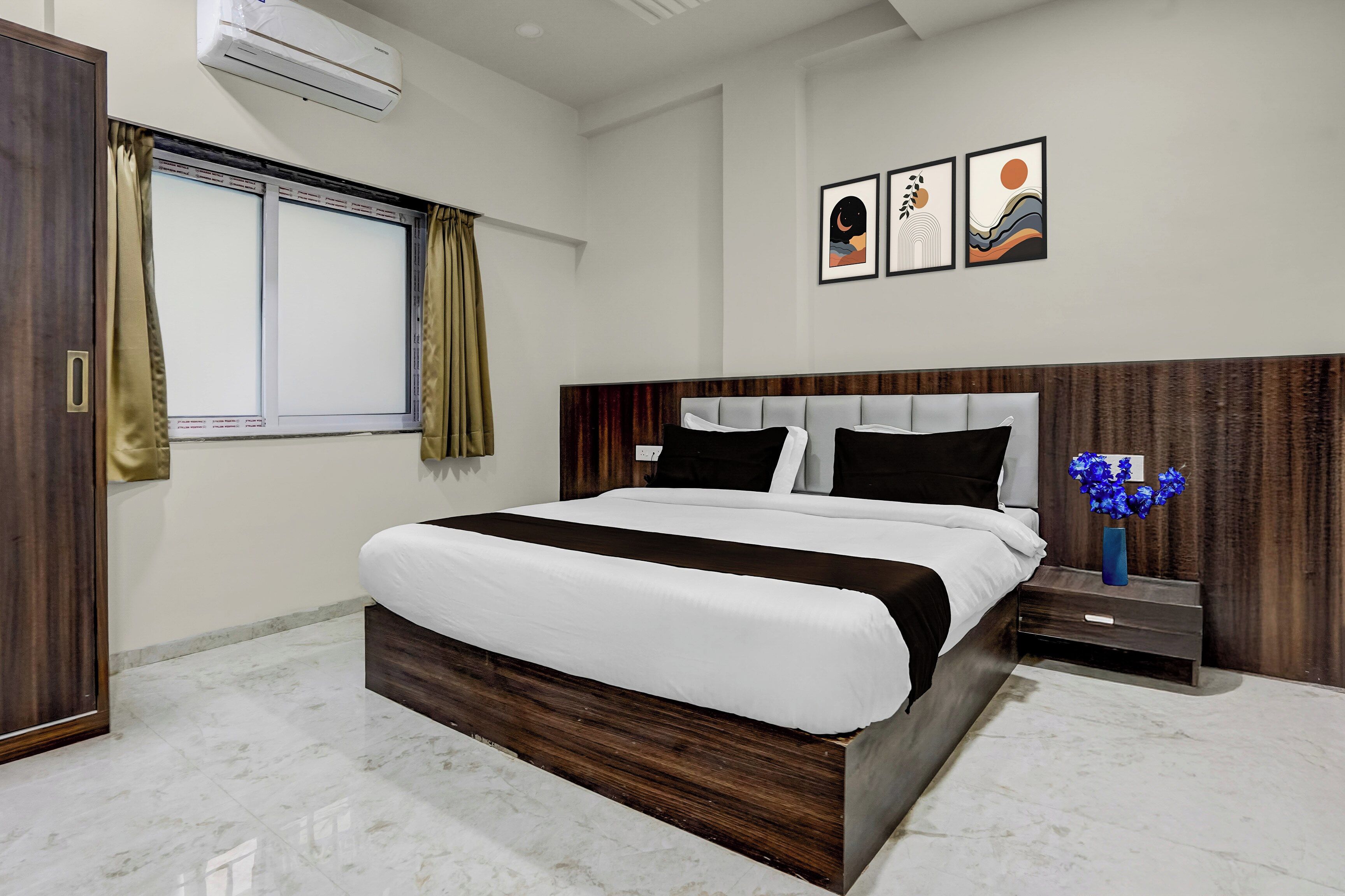 A modern hotel room with a large bed, a nightstand, a vase of flowers, and artwork on the wall.