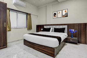 A modern hotel room with a large bed, a nightstand, a vase of flowers, and artwork on the wall.