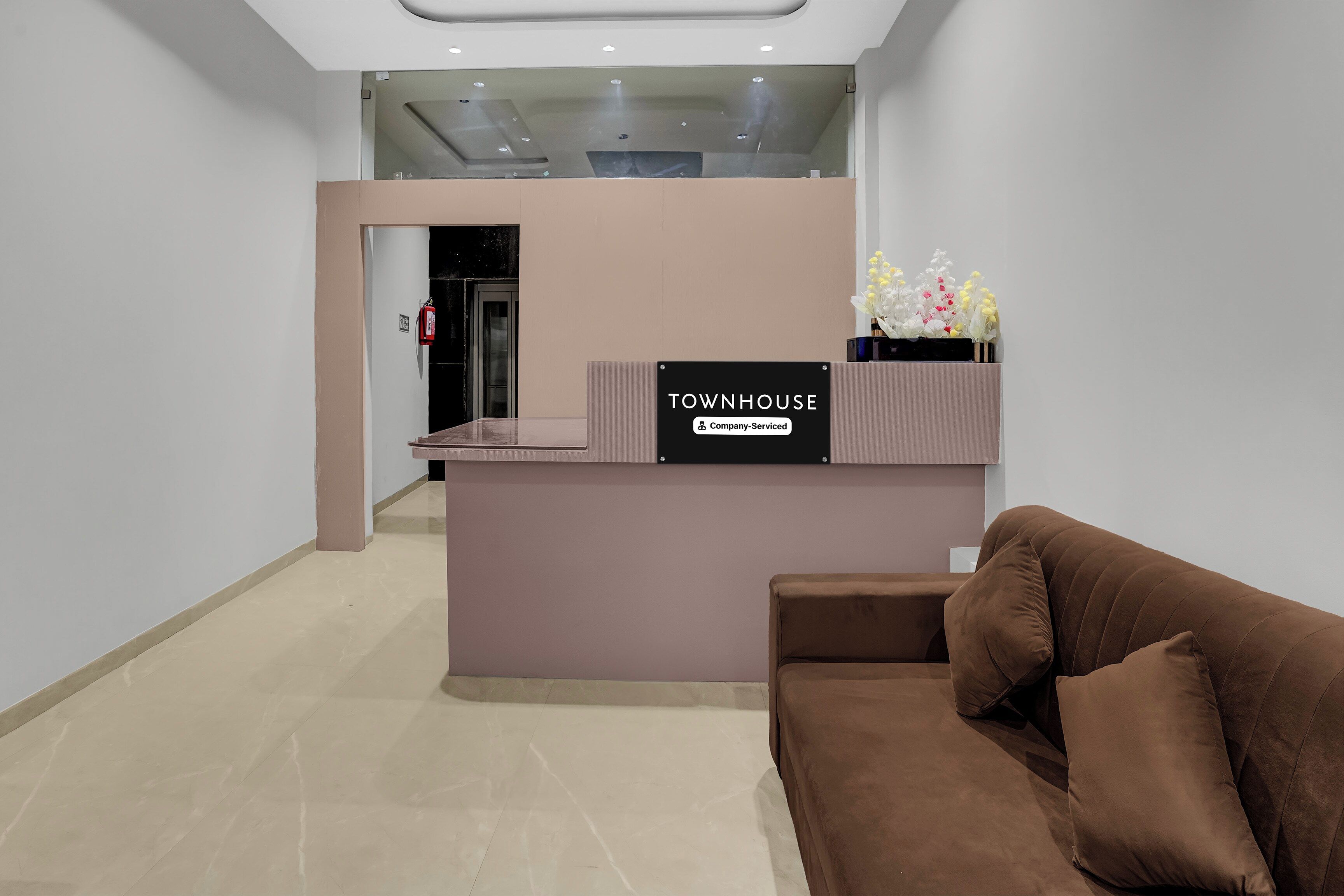 Un espace d’accueil comprenant un comptoir de réception, un canapé marron et un arrangement floral.