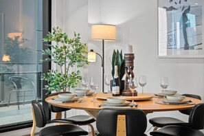 A dining area with a round table set for six, surrounded by black chairs. There is a potted plant to the left, a floor lamp, and a candelabra on the table. - Southbank Balcony 3 Bedroom (Southbank)
