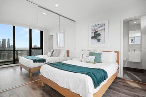 A modern hotel room with two beds, a large window with a city view, a framed picture on the wall, and a bathroom with a mirror and sink. - Southbank Balcony 3 Bedroom (Southbank)