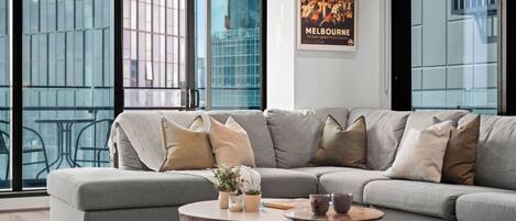 A modern living room with a grey sectional sofa, a round coffee table, and a poster of Melbourne.