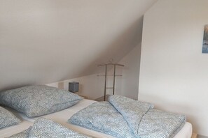 Ein Schlafzimmer mit schrägen Wänden, einem Bett mit gemusterten Betttextilien, einem Nachttisch und einem Wandregal.
