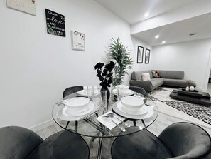 A modern dining area with a glass table set for four, surrounded by dark chairs. - Premium, Family-friendly 2-bedroom Private Suite (Calgary)