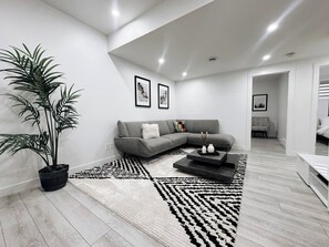 A modern living room with a grey sectional sofa, a black and white patterned rug, and a large potted plant. - Premium, Family-friendly 2-bedroom Private Suite (Calgary)