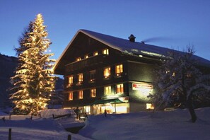 Ein mehrstöckiges Hotel mit verschneitem Dach, beleuchteten Fenstern und einem sichtbaren Schild.