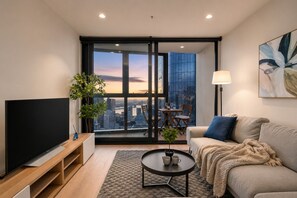 A modern living room with a large TV, a sofa, a coffee table, and a balcony with a city view. - Sky High 3 Bedroom City Stay (Melbourne)