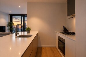 A modern kitchen with a large window, a sink, a stove, and a potted plant. - Sky High 3 Bedroom City Stay (Melbourne)