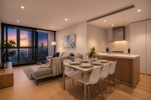 Un salon moderne comprenant un coin repas, de grandes fenêtres offrant une vue sur la ville, une cuisine avec un plan de travail et un canapé donnant sur le paysage.