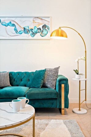 A teal sofa with patterned pillows, a gold floor lamp, and a white coffee table with two white mugs. - Port Melbourne 4 Bedroom Home (Port Melbourne)