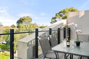 A balcony with a glass table, two chairs, a bottle of wine, and a potted orchid. - Port Melbourne 4 Bedroom Home (Port Melbourne)