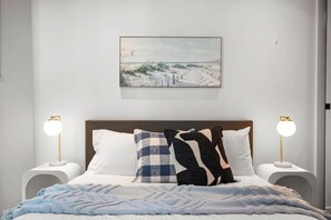 Ein Schlafzimmer mit einem Bett, zwei Nachttischlampen, einem Wandbild und einer blauen Decke.