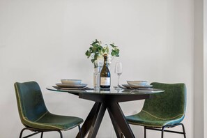 A dining table with two chairs, a bottle of wine, and a vase with flowers. - Modern 1 Bedroom City Escape (Melbourne)