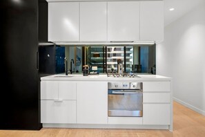 A modern kitchen with white cabinetry, a stainless steel oven, and a black refrigerator. - Modern 1 Bedroom City Escape (Melbourne)
