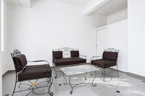 A room with a white wall, a glass coffee table, and two brown upholstered chairs with metal frames.