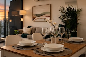 Une table à manger dressée avec des assiettes, des verres et un vase rempli de fleurs, avec un canapé et une lampe en arrière-plan.