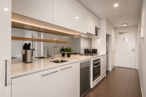 A modern kitchen with white cabinets, stainless steel appliances, and a built-in oven. - 27th Floor Flagstaff 2 Bedroom (Melbourne)