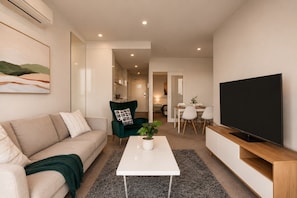 A modern living room with a sofa, a green armchair, a coffee table, and a TV. - 27th Floor Flagstaff 2 Bedroom (Melbourne)