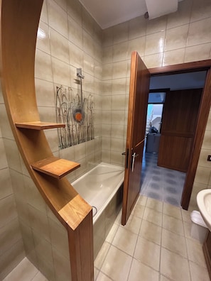 Un bagno con una vasca, uno scaffale in legno e una zona doccia.