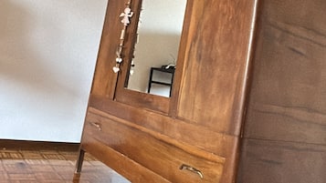 Een houten kast met spiegel, een lade en een klein tafeltje op de achtergrond.