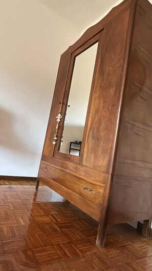 Un armario de madera con espejo, un cajón y una pequeña mesa al fondo.
