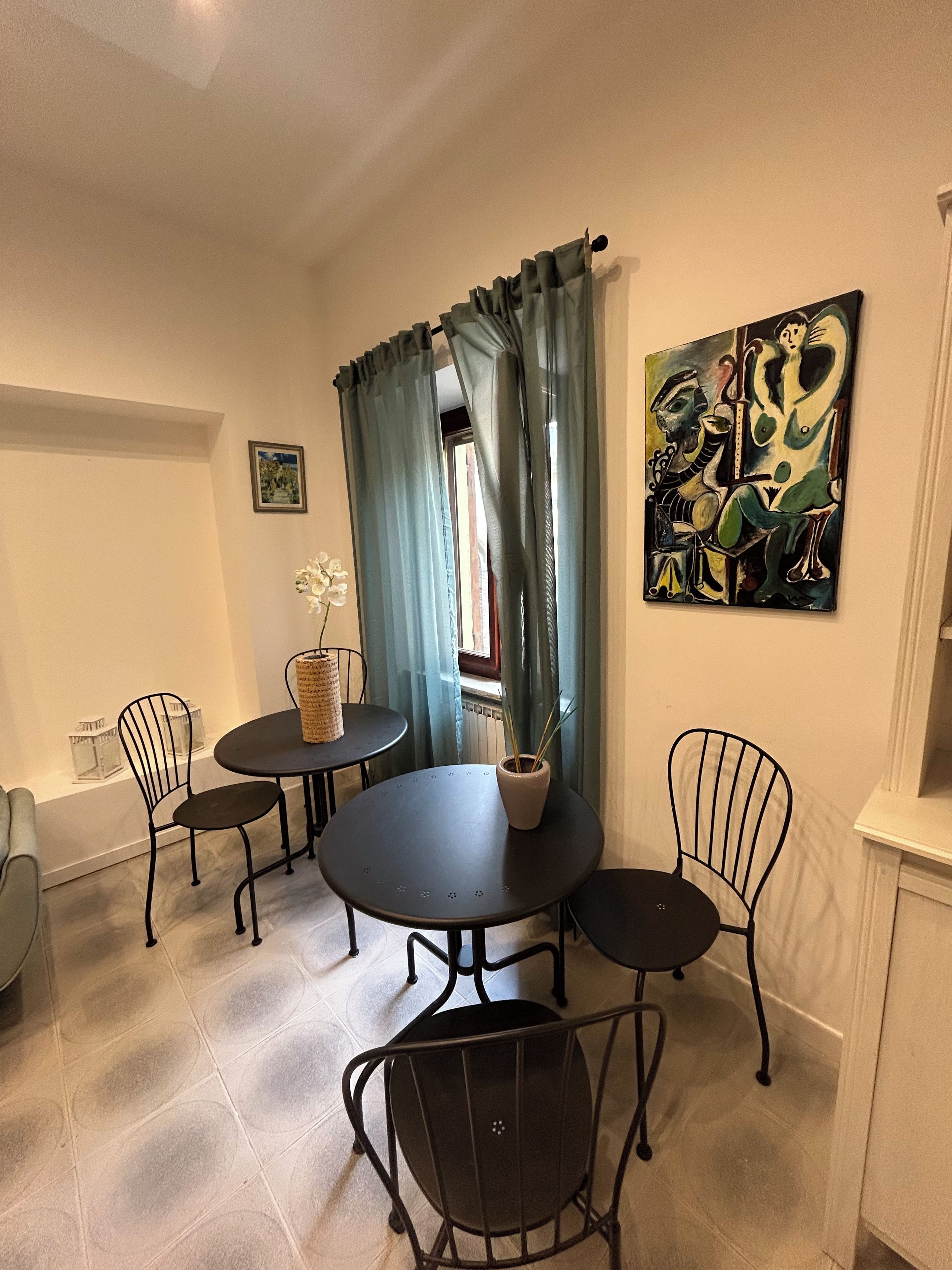 Zona pranzo con tavolo rotondo, quattro sedie, un vaso con una pianta e un quadro appeso al muro.