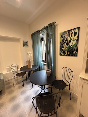 Zona pranzo con tavolo rotondo, quattro sedie, un vaso con una pianta e un quadro appeso al muro.