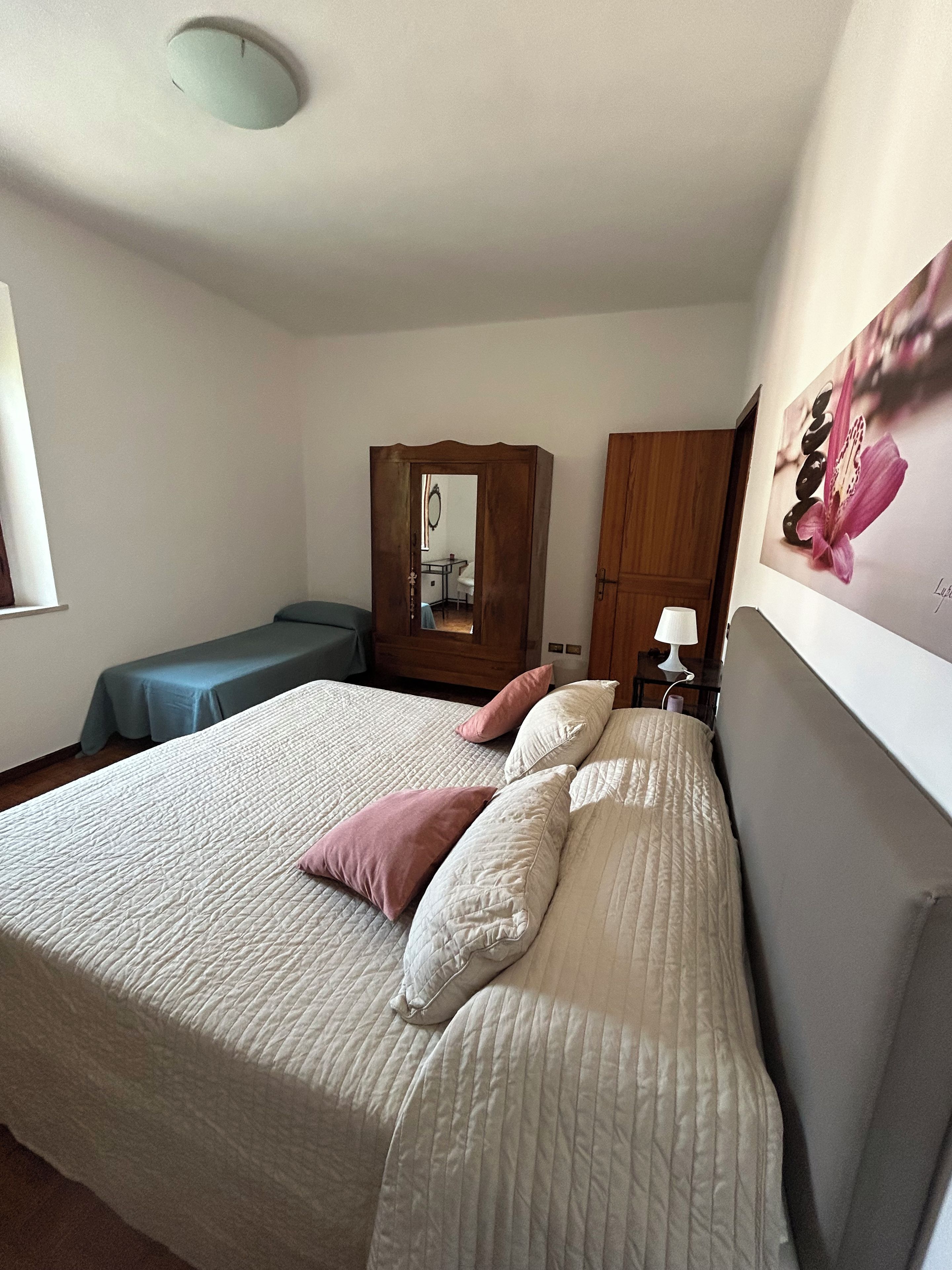 Una camera da letto con un letto, cuscini, un armadio, una scrivania e uno specchio.