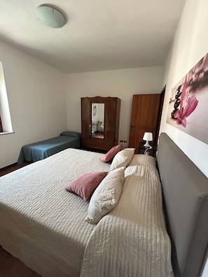 Una camera da letto con un letto, cuscini, un armadio, una scrivania e uno specchio.