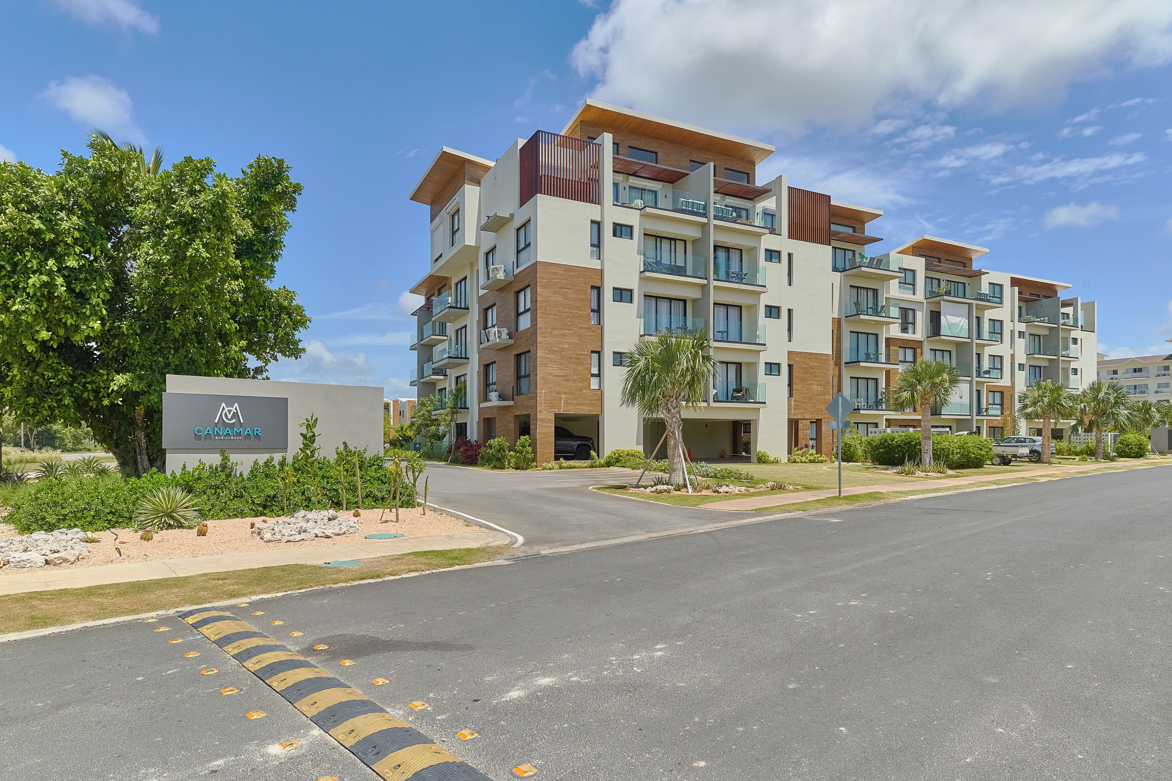 A multi-story hotel with a modern design, featuring balconies, a landscaped entrance, and a clear sky.
