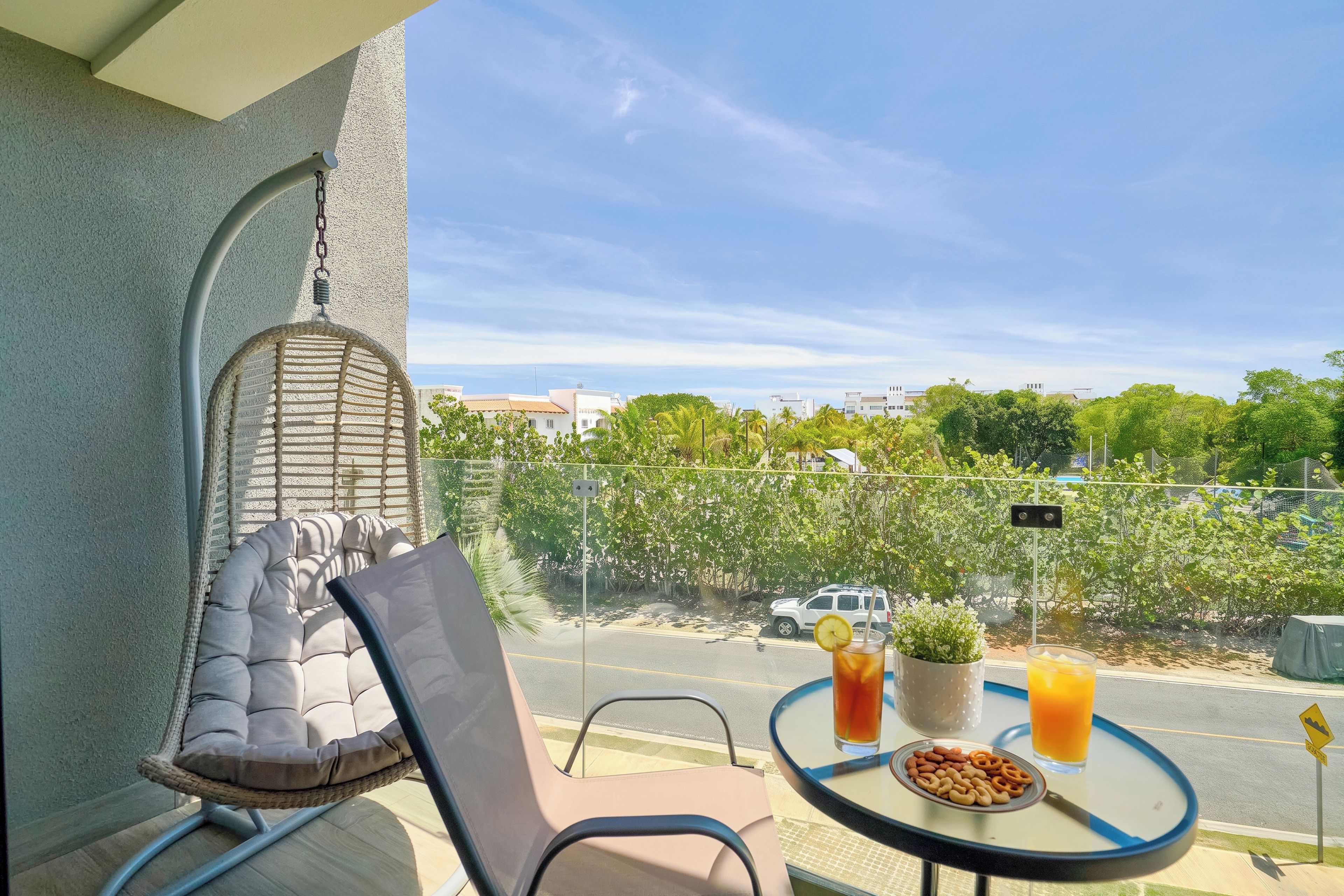 Un balcon avec un fauteuil confortable, une table avec des collations et des boissons, et une vue sur la rue et la verdure.