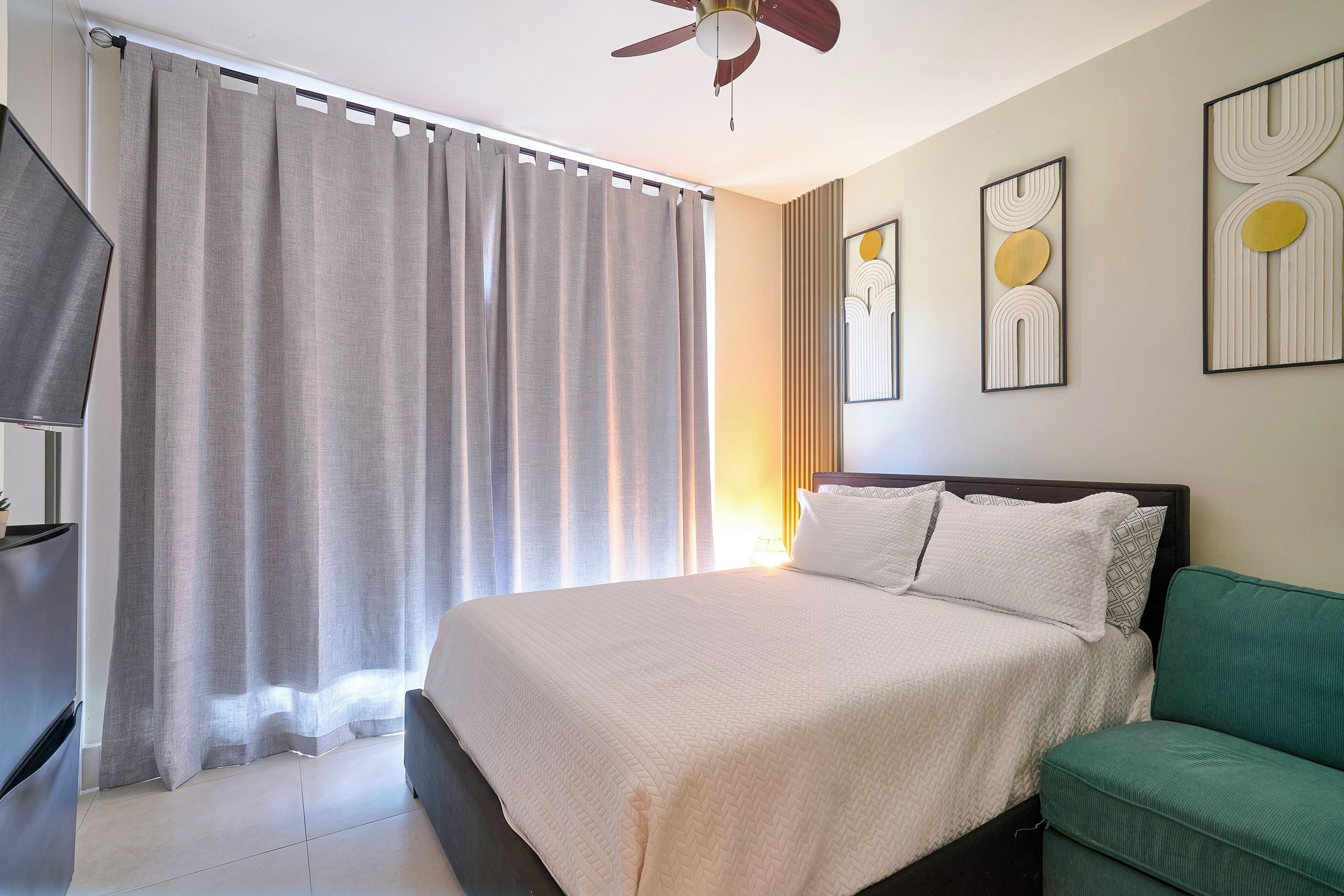 A hotel room with a bed, a green sofa, a ceiling fan, and artwork on the walls.