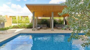 A swimming pool with a wooden pergola, lounge chairs, and a stone wall in the background.