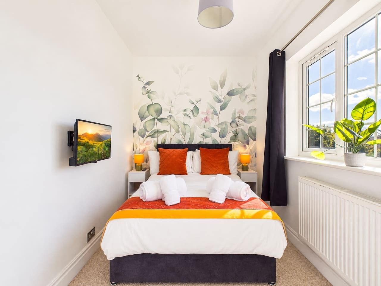 Ein Hotelzimmer mit einem Bett, einem an der Wand befestigten Fernseher, einem Fenster mit Ausblick und einer Zimmerpflanze.