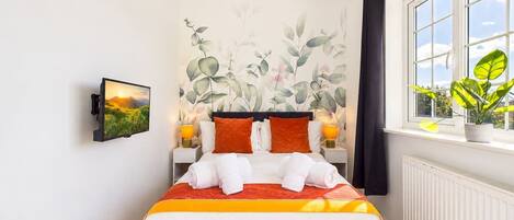 A hotel room with a bed, a wall-mounted TV, a window with a view, and a potted plant.
