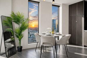 A modern dining area with a city view, a large mirror, and a potted plant. - Stadium Side 2 Bedroom Retreat (Docklands)