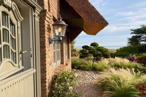 A brick building with a white door and a thatched roof. - Holiday home in Kampen with swimming pool (Kampen)