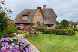 A traditional thatched-roof house with a brick facade, surrounded by a well-maintained garden with various flowering plants. - Holiday home in Kampen with swimming pool (Kampen)