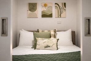 A bed with white bedding, a green knitted throw, and three wall art pieces above it. - Serene 2 Bedroom with Parking (Melbourne)