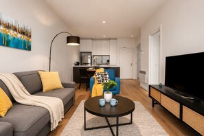 Una sala moderna con sofá, mesa de centro, televisor y una cocina al fondo.