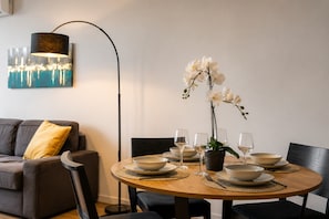 Una mesa de comedor dispuesta con platos, tazones y copas de vino, una orquídea en maceta y una lámpara de pie moderna.