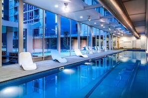 A modern indoor swimming pool with clear glass walls, lounge chairs, and a view of the outside. - Serene 2 Bedroom with Parking (Melbourne)