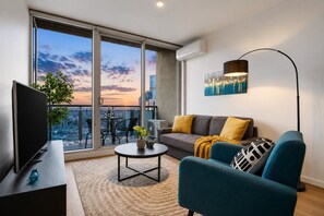 A modern living room with a sofa, coffee table, and a TV. - Serene 2 Bedroom with Parking (Melbourne)