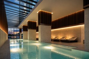 A modern indoor pool area with a glass ceiling, lounge chairs, and wooden paneling. - 70th Floor City View Apartment (Melbourne)