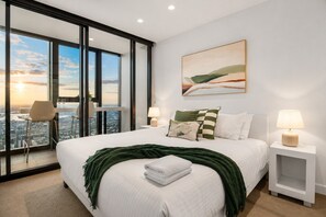 A modern hotel room with a large bed, a city view, a dining area, and a painting on the wall. - 70th Floor City View Apartment (Melbourne)