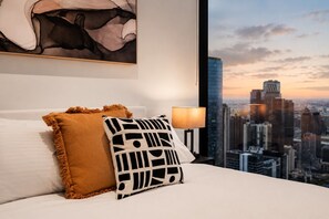 A hotel room with a bed, a city view, a lamp, and a painting on the wall. - 70th Floor City View Apartment (Melbourne)