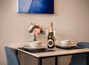 A dining table with a bottle of champagne, two bowls, and a vase of flowers. - Cozy Docklands 1 Bedroom (Docklands)