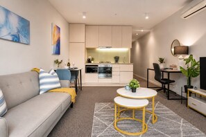 A modern living room with a sofa, a coffee table, and a dining area with a chair and a table. - Cozy Docklands 1 Bedroom (Docklands)