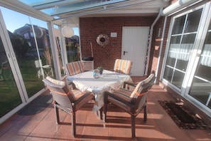 An outdoor patio with a table and chairs, a brick wall, and a door. - Oysterfinders (1230) (Neßmersiel)